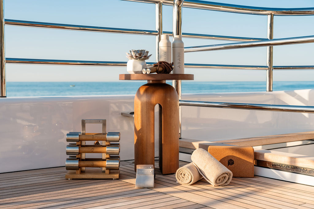 Paragon dumbbells, side table, towels and cork yoga block on a superyacht's teak deck, with the sea beyond